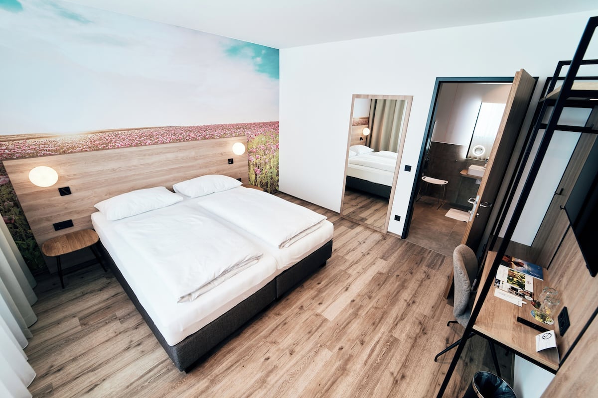Une chambre d’hôtel moderne, dotée d’un grand lit, d’un bureau et d’une salle de bain visible à travers une porte ouverte.