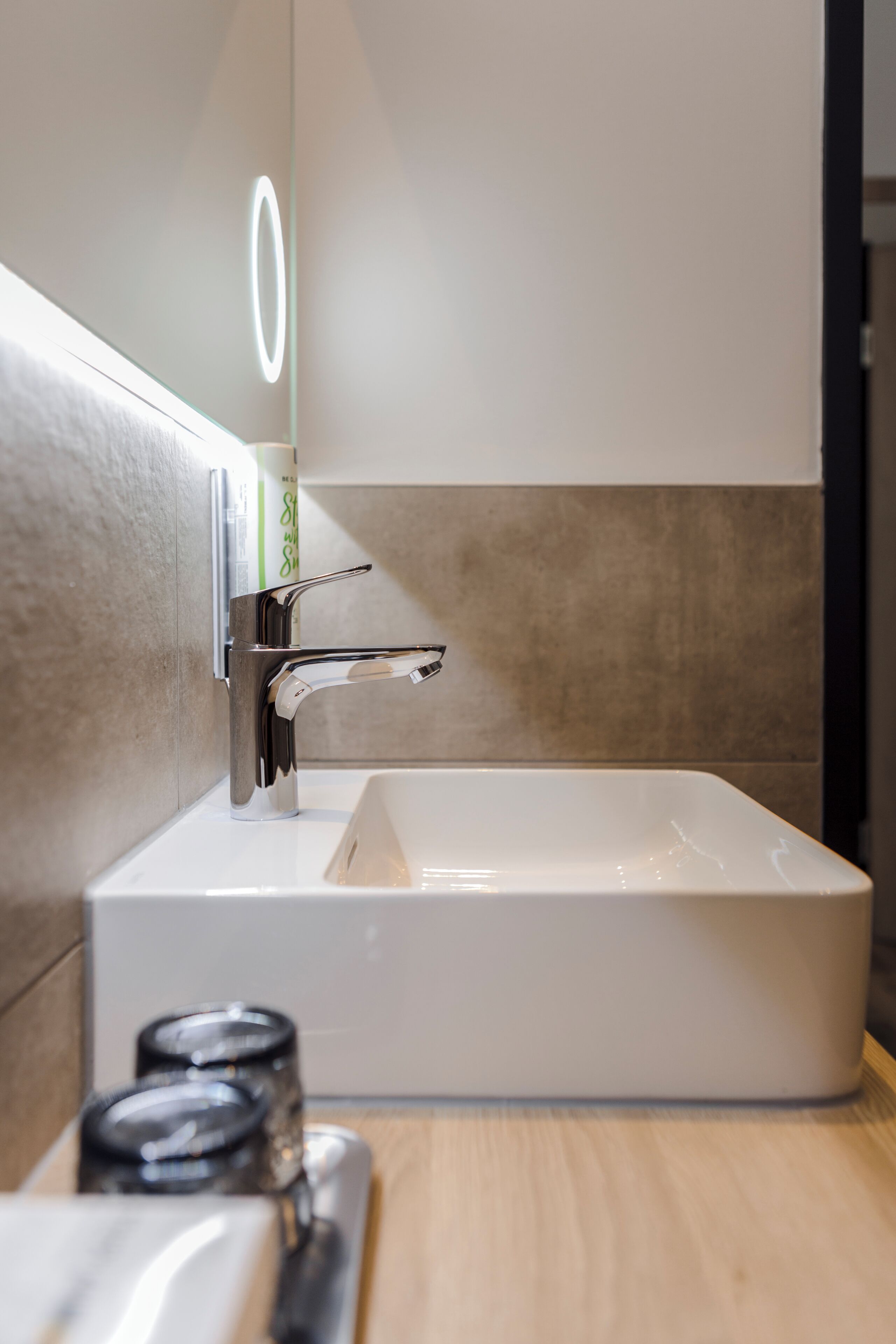 Un baño moderno con grifo cromado, un lavamanos rectangular y un espejo con luz. Hay dos frascos en la encimera.