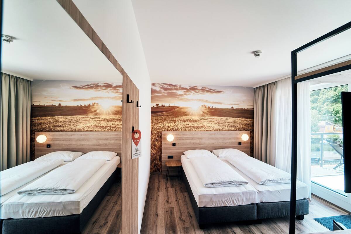 Une chambre d’hôtel avec deux lits, des têtes de lit en bois et une fresque représentant un paysage au coucher du soleil.