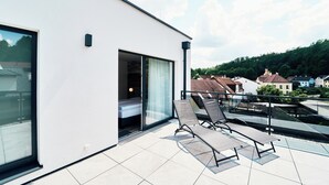 Een modern gebouw met een balkon, voorzien van twee loungestoelen en een glazen deur naar een slaapkamer.