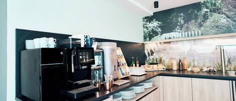 A modern coffee station with a coffee machine, cups, and a menu board.