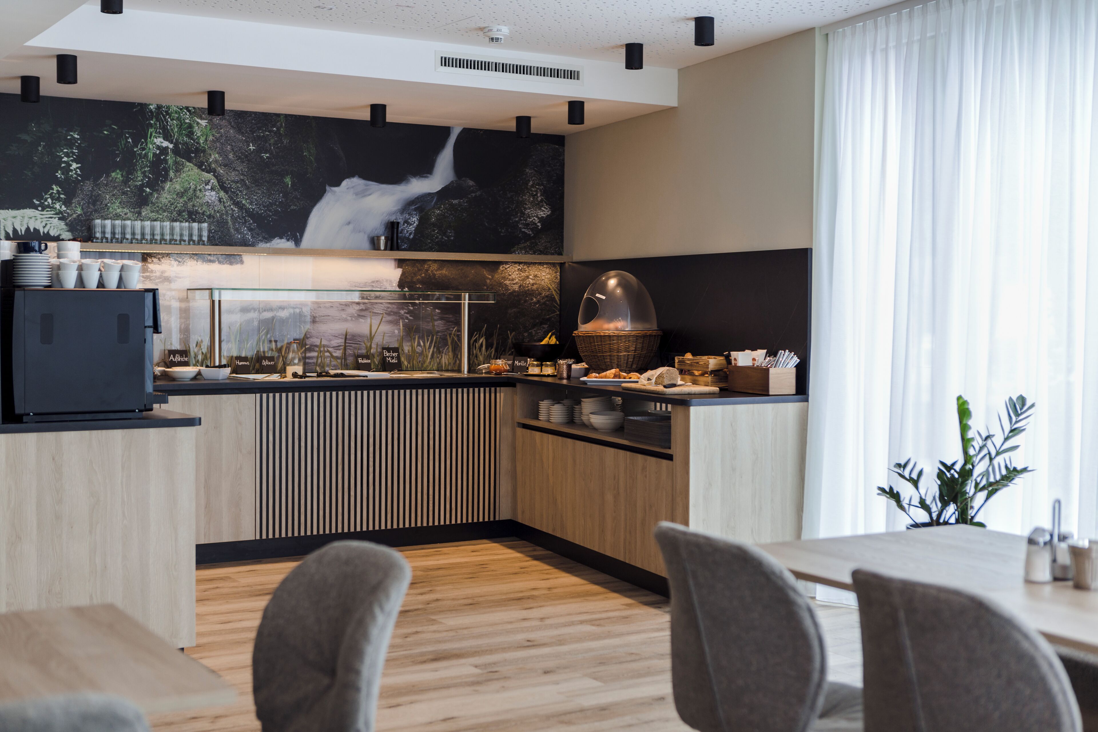 Una cocina moderna con un mural tipo cascada, armarios de madera y un comedor con sillas grises.