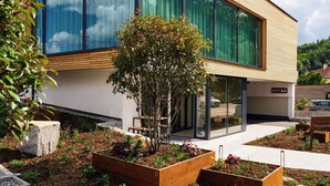 Een modern hotel met een grote glazen gevel, een gastvrij bord en een aangelegde tuin.