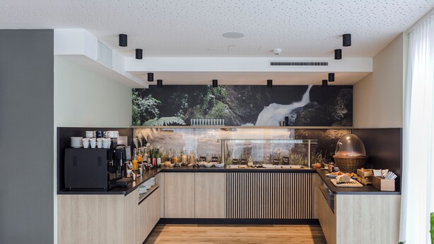Een moderne keuken met een centraal eiland, ingebouwde apparatuur en een groot raam met uitzicht op een tuin.