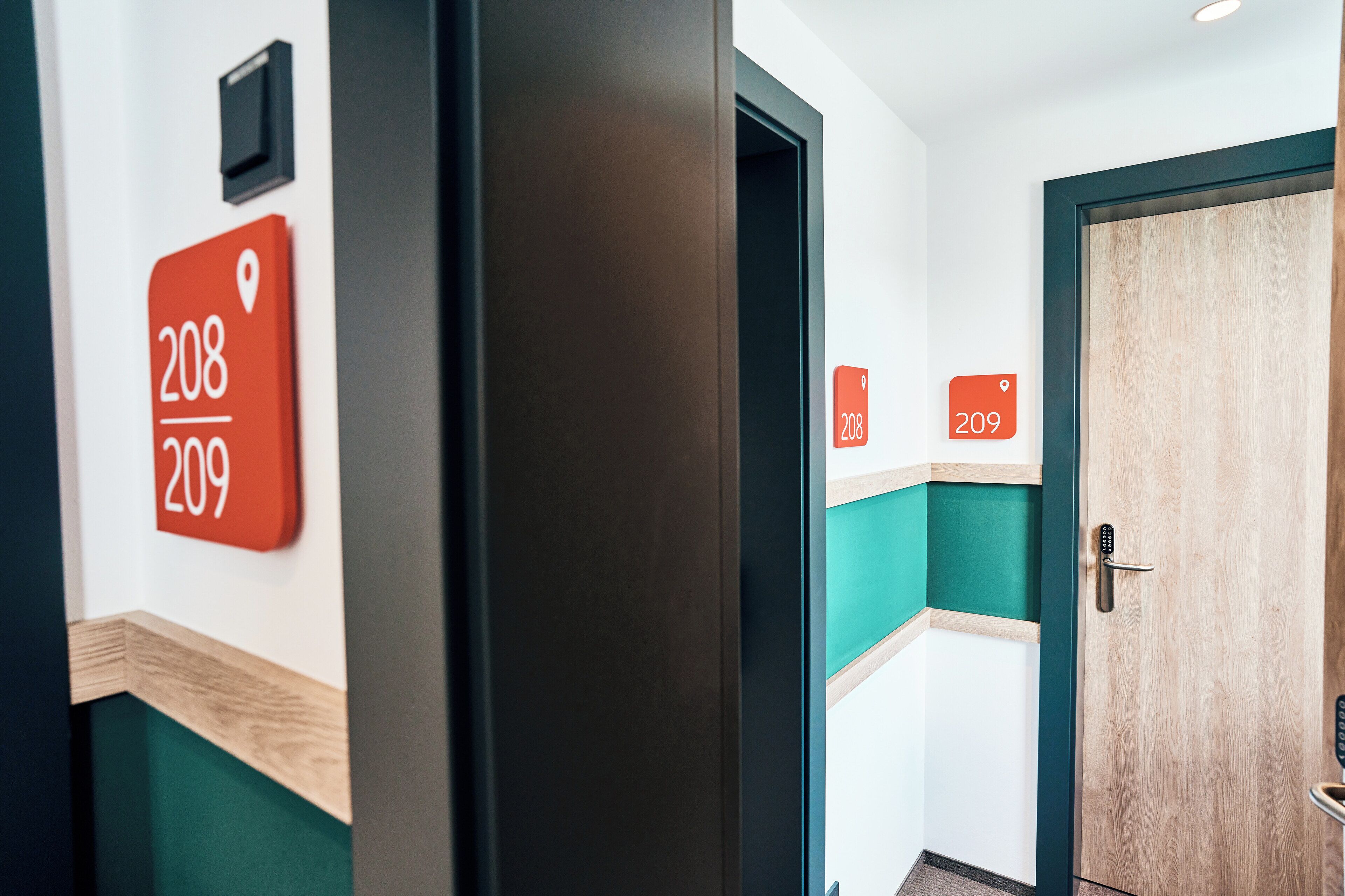 A hallway with a wooden door, teal and white walls, and numbered signs indicating room 208 and 209.