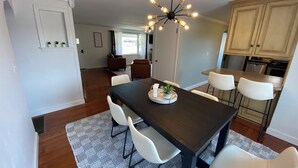 Un comedor con mesa de madera oscura, sillas blancas y una lámpara de techo moderna.