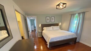 Un dormitorio con suelo de madera, una cama con ropa de cama blanca, una mesita de noche con lámpara y un aplique de techo.