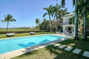 A swimming pool with a clear blue water surface, surrounded by a well-maintained lawn and palm trees.