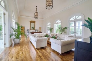 A spacious room with a wooden floor, white sofas, a billiards table, and large windows.