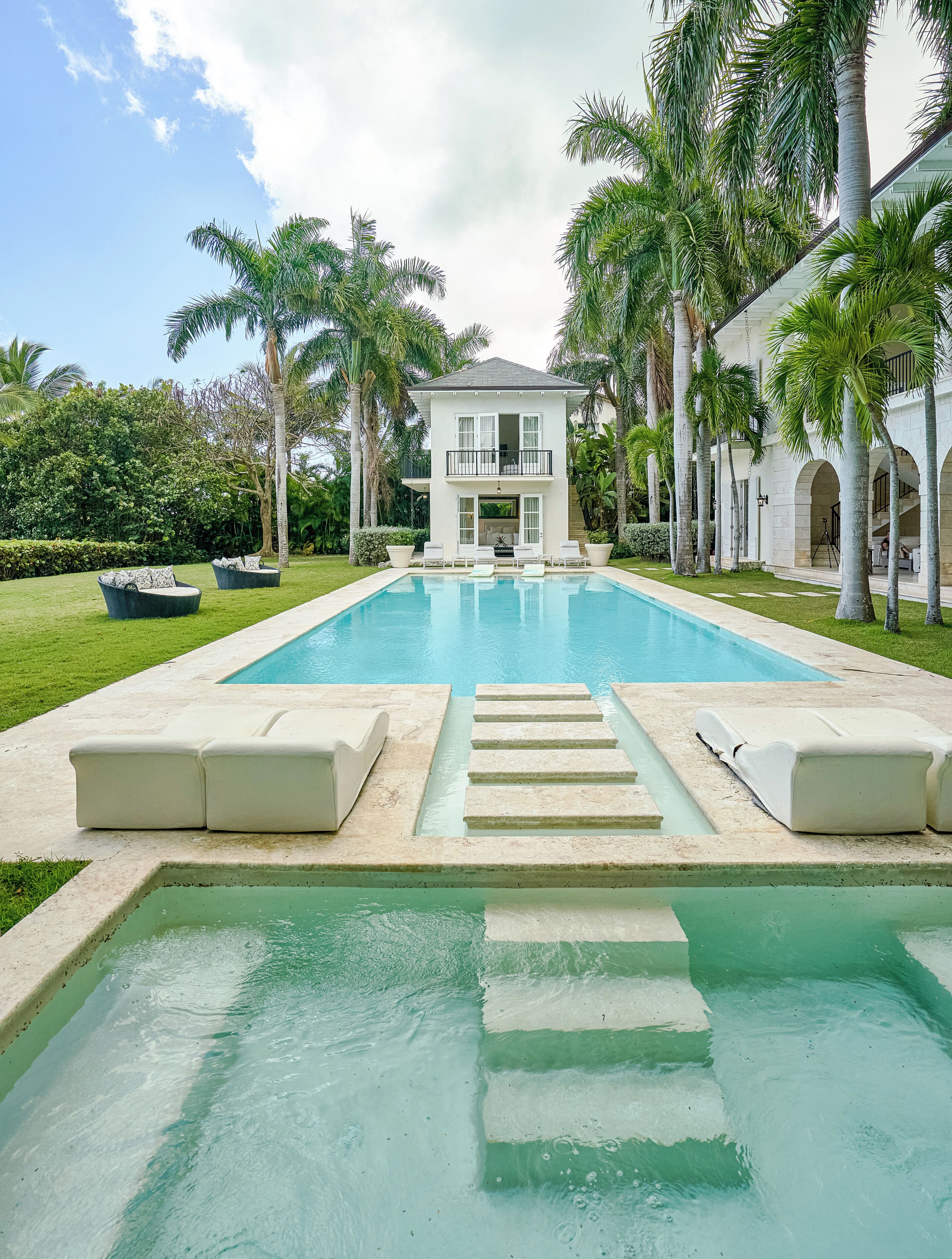 A two-story house with a swimming pool, surrounded by palm trees and a well-maintained lawn.