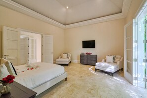 A bedroom with a large bed, two chairs, a dresser, and a TV on the wall. - Luxurious Ocean and Golf View Villa staffed with Private Chef, Butler and Maid! (Punta Cana)