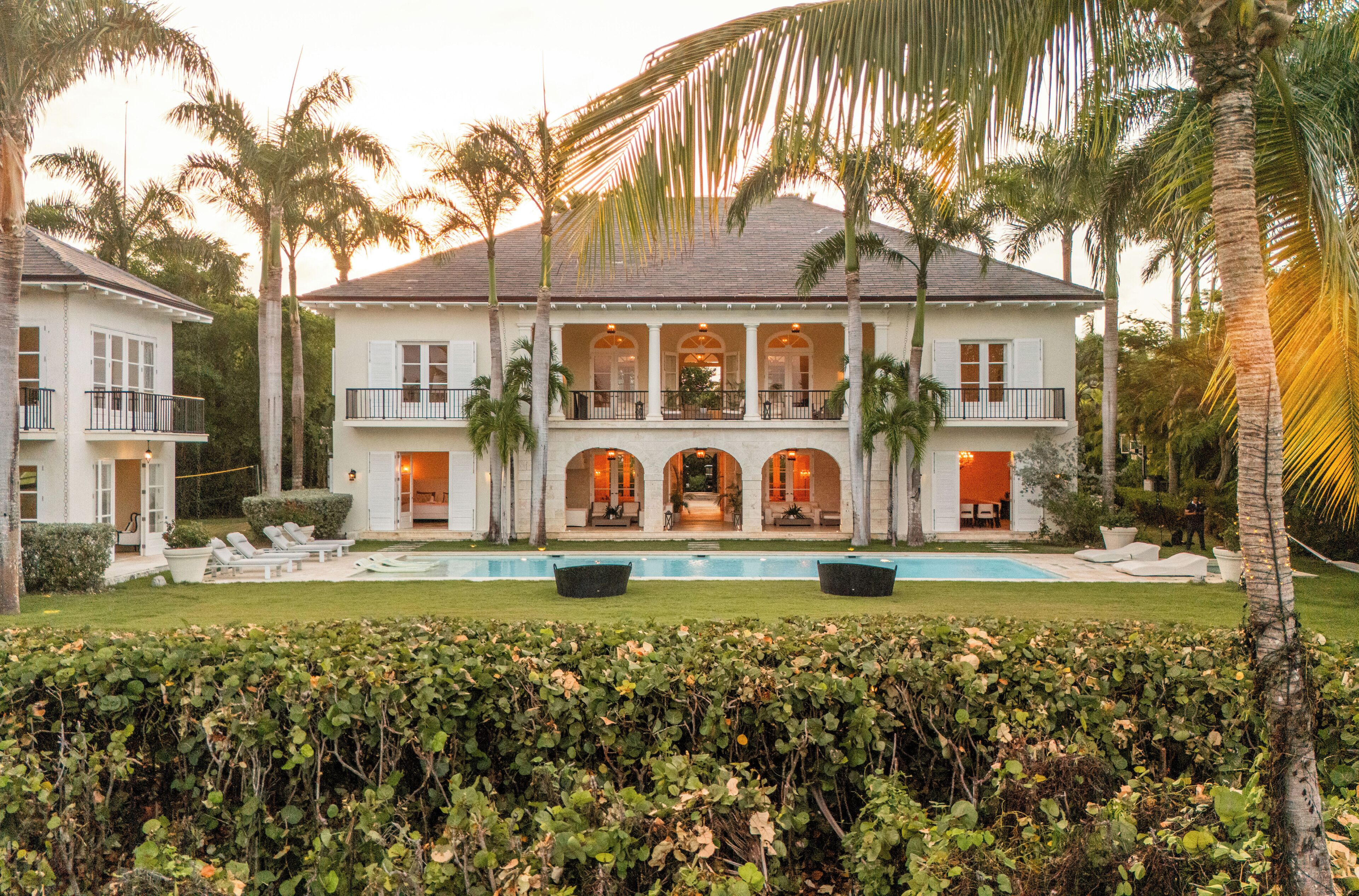 A two-story house with a swimming pool, multiple balconies, and palm trees.