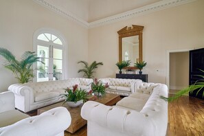 Un salon spacieux avec un grand canapé d’angle blanc, une table basse en bois et plusieurs plantes en pot.