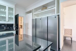 A modern kitchen with a large stainless steel refrigerator, white cabinetry, and a glass-top island. - Luxurious Ocean and Golf View Villa staffed with Private Chef, Butler and Maid! (Punta Cana)
