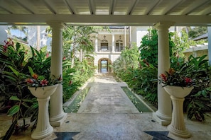 A covered walkway with columns, leading to a building with an arched entrance. - Luxurious Ocean and Golf View Villa staffed with Private Chef, Butler and Maid! (Punta Cana)