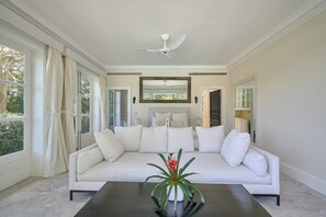 A modern living room with a white sofa, a ceiling fan, and a coffee table with a plant. - Luxurious Ocean and Golf View Villa staffed with Private Chef, Butler and Maid! (Punta Cana)