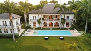 A large two-story house with a swimming pool, multiple balconies, and lush greenery.