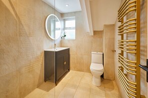 A modern bathroom with a dark vanity, a white toilet, and a gold towel rack.
