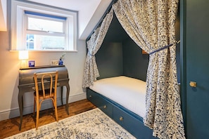 A bedroom with a canopy bed, a desk with a chair, a window, and a rug.