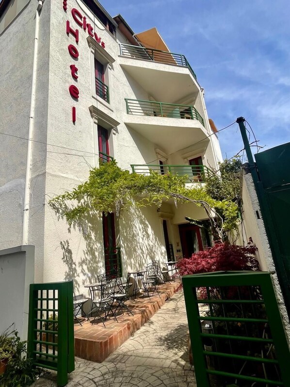 A hotel with a white facade, balconies, outdoor seating, and a gated entrance. - City 5 Hotel (Tirana)