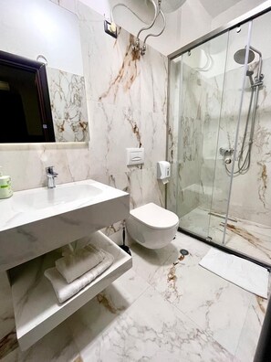 A bathroom with a marble floor, a white sink, a toilet, and a glass shower enclosure. - City 5 Hotel (Tirana)
