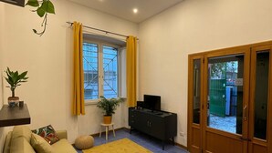 A living room with a sofa, a TV, a cabinet, and a window with yellow curtains. - Detached house in the heart of Chiaia (Napoli)