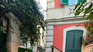 A courtyard with a cobblestone floor, a green gate, and a building with a red facade and green shutters. - Detached house in the heart of Chiaia (Napoli)