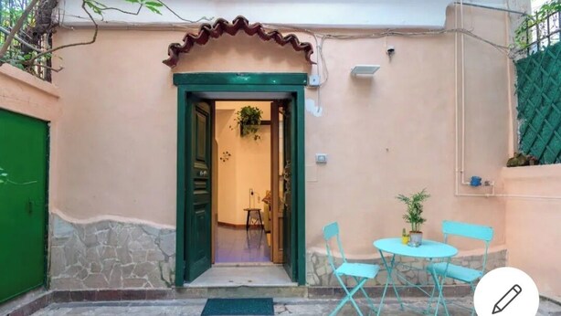 A building entrance with a green door, a small patio with a table and chairs, and a potted plant. - Detached house in the heart of Chiaia (Napoli)