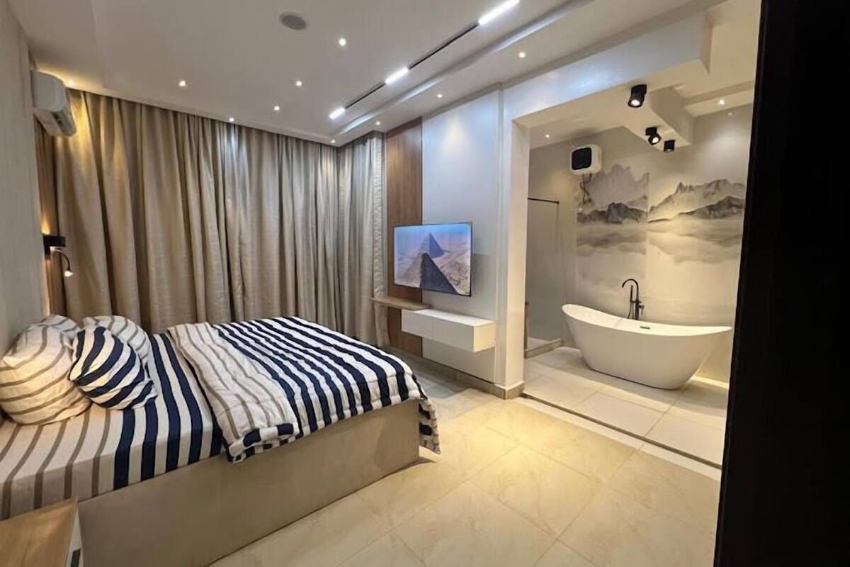 Una camera da letto moderna con un letto grande, una TV a parete e una vasca da bagno indipendente.