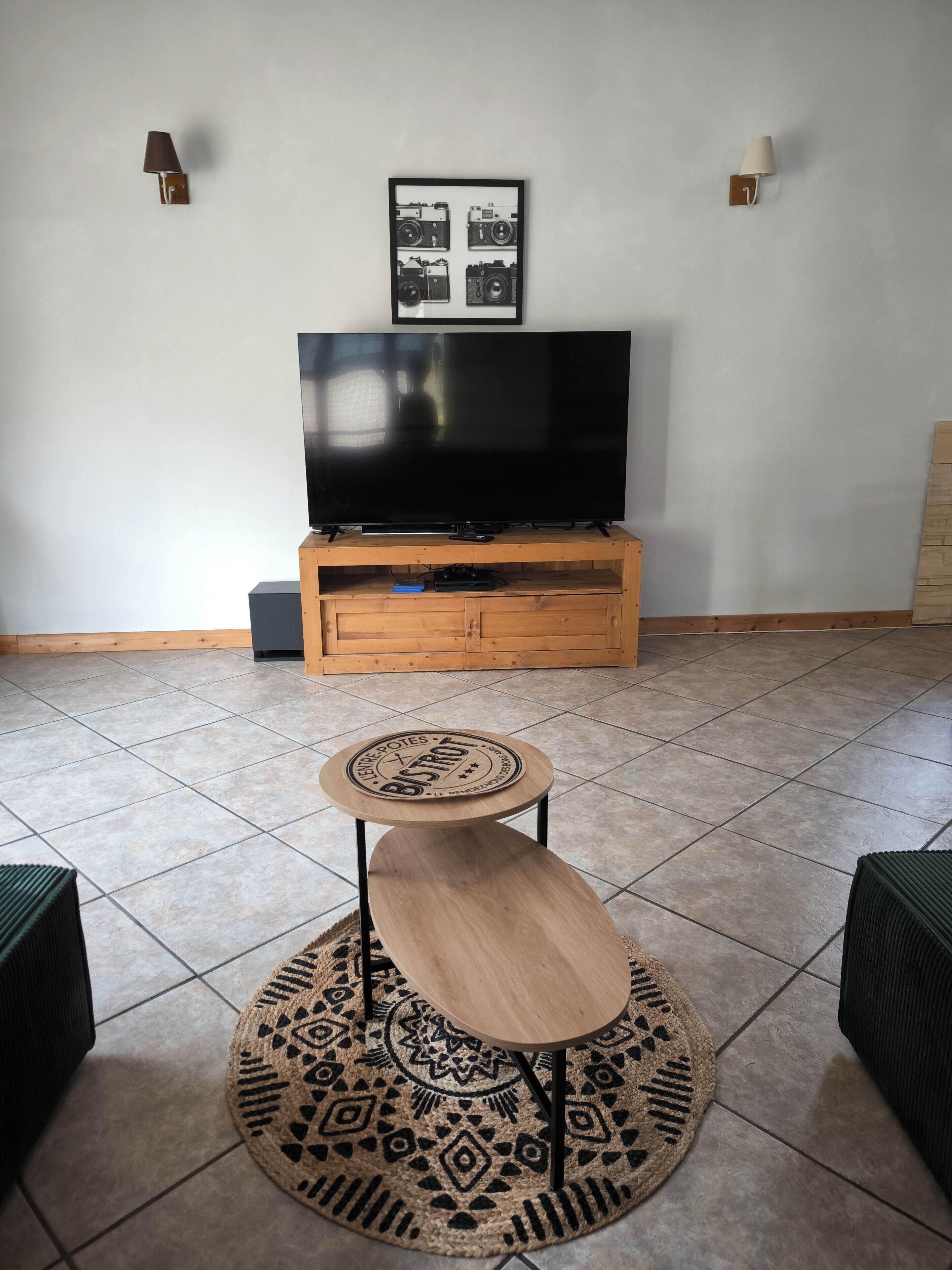 Una sala de estar con un televisor sobre un mueble de madera, una pequeña mesa redonda y una alfombra estampada.
