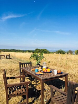 A wooden table set outdoors with a view of a field and distant hills.