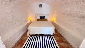 A narrow, arched room with a bed centered, flanked by two wall-mounted lamps. - Domaine de La Blache - The Vault (Saint-Jurs)