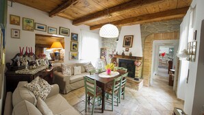 A cozy living room with a wooden ceiling, a fireplace, and a dining area with a table and chairs. - Flower Room (Marche)
