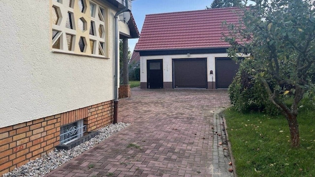 A residential driveway leading to a garage with a red roof, a white building with a window grille, and a small tree. - Breathing space-Spreewald (Vetschau/Spreewald)