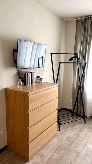 Una habitación con un aparador de madera, un televisor montado en la pared y un tendedero de metal negro.