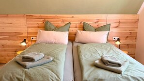Two twin beds with green bedding, pillows, and folded towels. Each bed has a wooden headboard and a bedside lamp. - Breathing space-Spreewald (Vetschau/Spreewald)