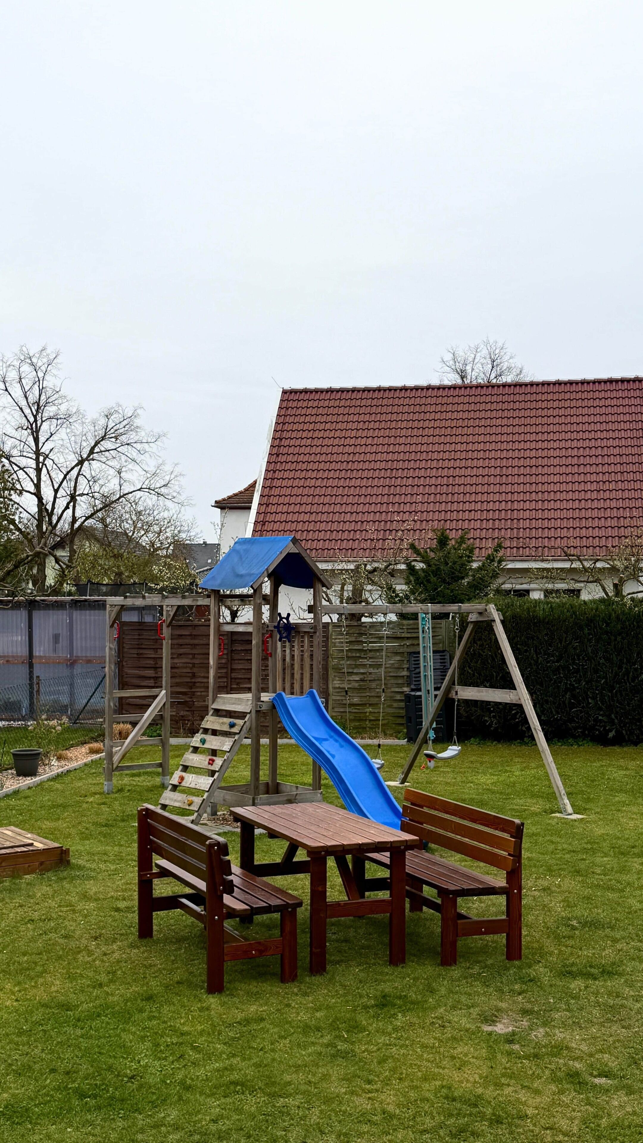 Ein Spielplatz mit Rutsche, Schaukeln und Picknicktischen in einem grünen Rasen.