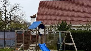 Ein Spielplatz mit Rutsche, Schaukeln und Picknicktischen in einem grünen Rasen.