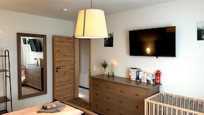 Un dormitorio con un aparador de madera, televisor, espejo y cuna.