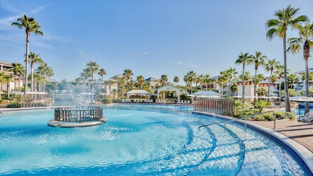 A swimming pool with a water fountain, surrounded by palm trees and lounge chairs. - 30A House with Pool and Bunk Rooms (Seacrest Beach)