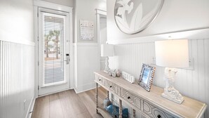 A hallway with a wooden console table, a round mirror, and a welcome sign. - 30A House with Pool and Bunk Rooms (Seacrest Beach)