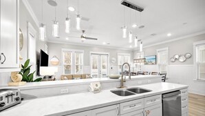 A modern kitchen with white cabinetry, a central island with a sink, and pendant lighting. - 30A House with Pool and Bunk Rooms (Seacrest Beach)