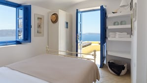 A bedroom with a bed, a view of the sea, a shelf with towels, and a basket. - Ilivatos - Elegant Villa on the Caldera's Edge (Oia)