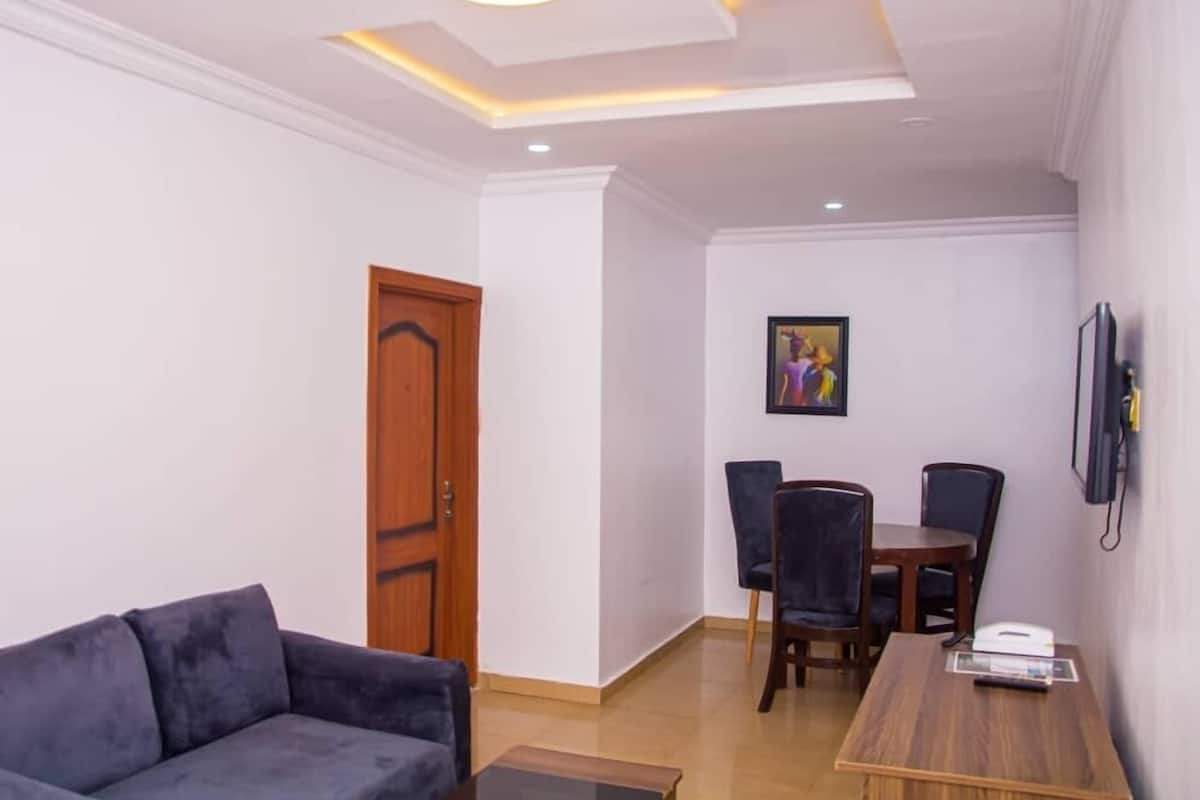 A modern living room with a sofa, a dining table with chairs, a wooden door, and a painting on the wall.