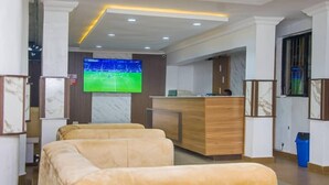 Et hotellobby med en receptionsdisk, et tv der viser en sportsbegivenhed, og to sofaer.