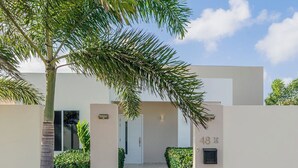 Entrada moderna de un edificio con un camino empedrado que lleva a una puerta, rodeada de follaje y un cielo despejado.