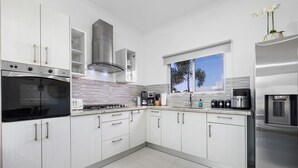 Una cocina moderna con armarios blancos, horno empotrado, estufa de acero inoxidable y ventana con vista a palmeras.