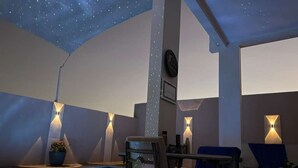 Zona de piscina con techo estrellado, sillones de descanso e iluminación en la pared.