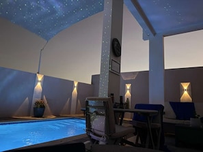 Zona de piscina con techo estrellado, sillones de descanso e iluminación en la pared.