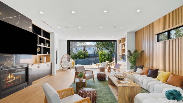 A modern living room with a fireplace, comfortable seating, and a large window offering a view of the outdoors. - Venice Open Designer House w Pool (Los Angeles)